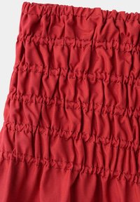 Section de tissu rouge avec plusieurs rangées de coutures élastiques rassemblées créant une texture froncée et un aspect ajusté.