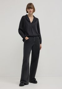 Blusa nera in satin con colletto e maniche lunghe, abbinata a jeans neri a zampa d'elefante e stivali neri chunky. Design semplice e moderno.