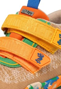 Gros plan d'une basket enfant colorée avec des bandes velcro orange et jaune, des accents verts et des logos de singe dessin animé sur les bandes et l'étiquette.