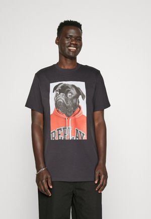 Camiseta negra con un gráfico central de un pug que lleva una sudadera roja con el texto "REPLAY", hecha de algodón suave, con cuello redondo y mangas cortas.