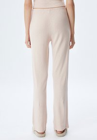 Lichtroze, geribbelde gebreide broek met een relaxte pasvorm en subtiele textuurdetails. Beschikt over een elastische tailleband en uitlopende pijpen.
