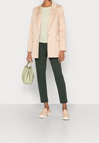 Lichtroze blazer, groene gemêleerde top, donkergroene tapse broek, beige instap schoenen en een zachte groene handtas. Minimalistisch ontwerp, casual uitstraling.