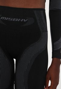 Černé sportovní legíny s texturovaným designem, které mají různé pruhované vzory a logo na pásku. Hladká, přiléhavá tkanina.