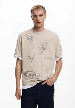 Beige sweatshirt with short sleeves, featuring intricate black sketches of birds and fish. Layered over a white t-shirt, paired with dark jeans.