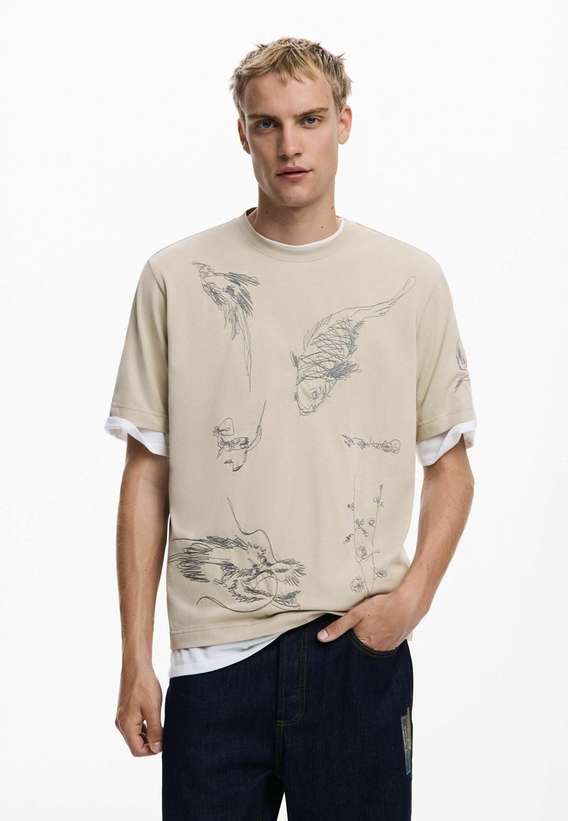 Beige sweatshirt with short sleeves, featuring intricate black sketches of birds and fish. Layered over a white t-shirt, paired with dark jeans.
