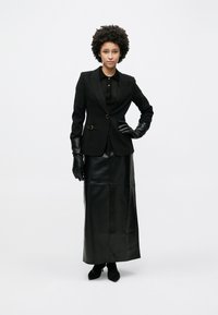 Μαύρο σακάκι με ραφή, με χρυσή λεπτομέρεια, συνδυασμένο με μαύρη δερμάτινη μακριά φούστα. Μαύρα γάντια και παπούτσια ολοκληρώνουν την εμφάνιση.