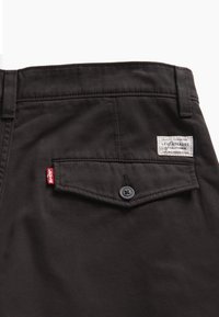 Zwarte katoen broek met een achterzak met knoopsluiting en een wit label met de tekst "Levi Strauss". Gladde stoftextuur.