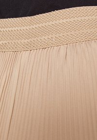 Plisserad kjol i beige tyg med ett vävt elastiskt midjeband. Strukturerad yta med fina vertikala linjer och subtil lyster.