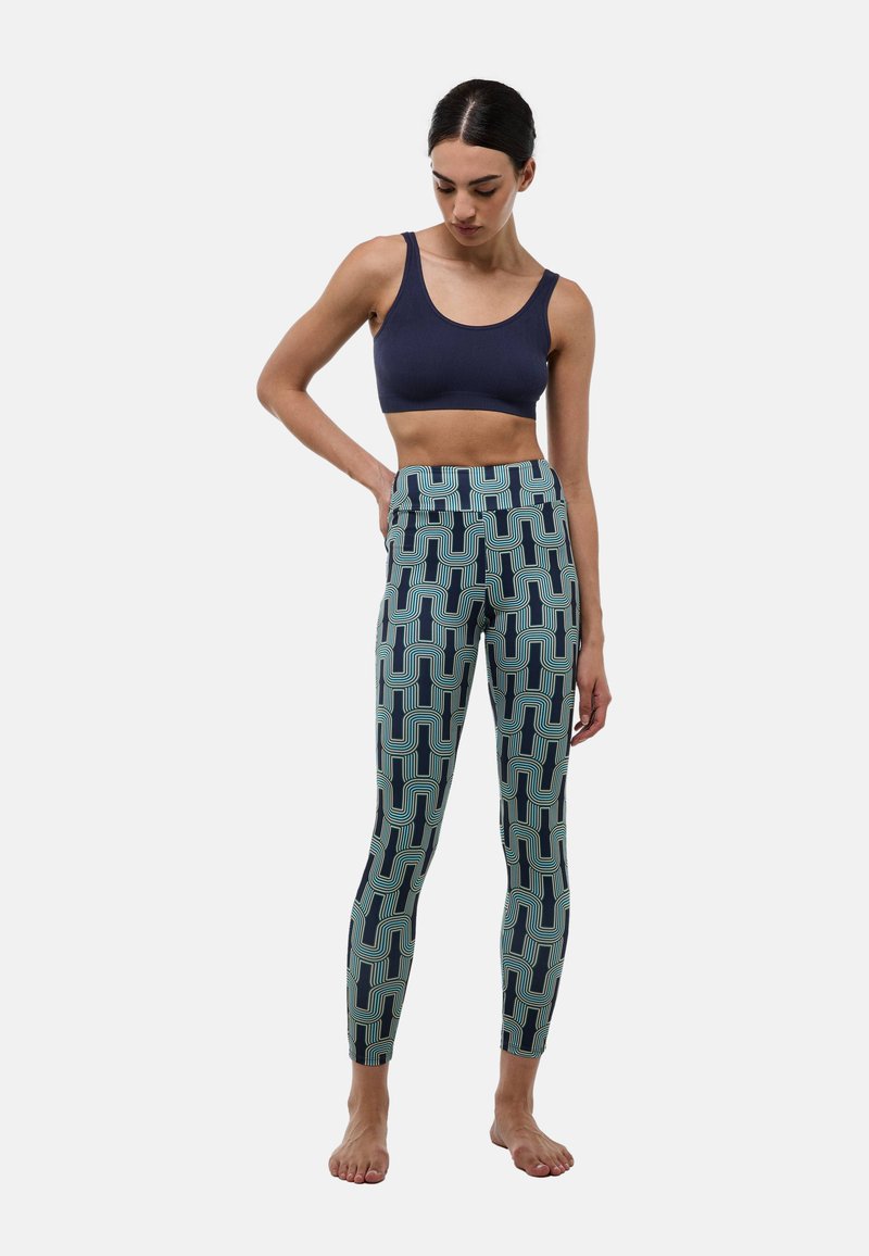 Brassière de sport bleu marine associée à des leggings à motif avec un design géométrique bleu et vert. Les leggings sont moulants avec une taille haute.