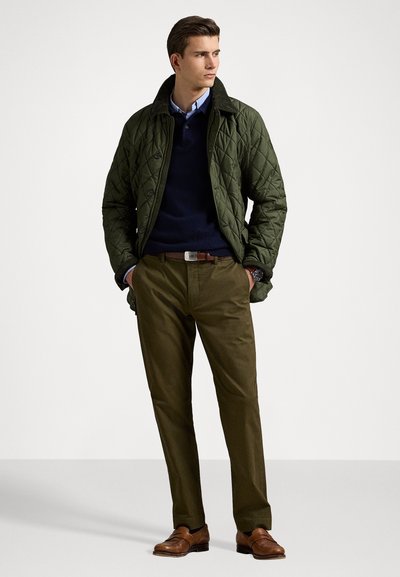 Green quilted jacket with a dark collar, navy sweater, tan chinos, and brown shoes. Key features include buttons and a textured fabric.