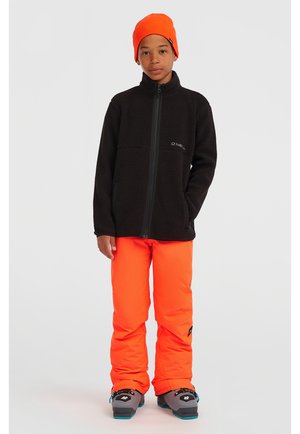 Svart fleecejacka med hög krage, dragkedjestängning och sidofickor, kombinerad med knallorange snöbyxor och grå kängor med blå detaljer.