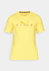 Žluté sportovní tričko s krátkým rukávem vyrobené z lehkého materiálu. Obsahuje logo "HYROX" a grafiku skákajícího pumy. Hladký povrch.