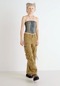 Korzet z denimu bez ramínek, khaki cargo kalhoty s kapsami a cihlové klobouky s leopardím vzorem. Hladký materiál a volný střih s viditelnými švy.