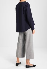 Marinblå långärmad topp med lös passform, kombinerad med ljusgrå vida byxor. Svarta platta skor fulländar outfiten. Minimalistisk design.