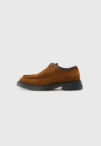 Zapato de ante marrón con cordones, suela negra y punta redondeada, con costuras en la parte frontal y tacón bajo, visto de lado.