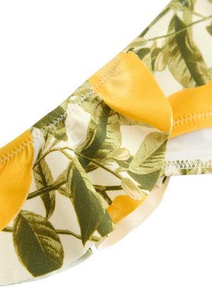 Keltainen ja valkoinen kangas, jossa vihreä lehtikuvio ja röyhelöreuna, sauman kohdalla tarkka ommel.