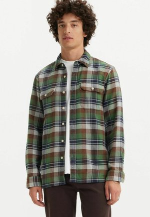 Green and brown plaid flannel shirt with two chest pockets, button-up front, and long sleeves. Features a soft texture and casual fit.