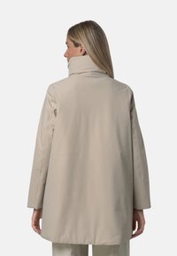 Beżowy płaszcz z długim rękawem i wysokim kołnierzem, wykonany z gładkiego, wodoodpornego materiału; ma prosty krój i minimalistyczne przeszycia.