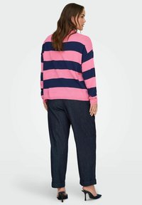 Różowo-granatowy sweter w paski o luźnym kroju, zestawiony z ciemnoniebieskimi spodniami dżinsowymi i czarnymi szpilkami. Prosty design, miękka faktura.