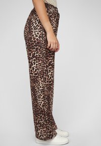 Leopardprintbroek met een ontspannen pasvorm, elastische tailleband en een gladde stof, gecombineerd met witte sneakers.