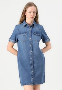 Jeanskjortekjole i mellomblå, med korte rullede ermer, krage, frontlukking med knapper og to brystlommer. Standard passform og lengde.