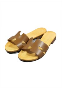 Sandali a scivolo in pelle marrone con una fascia larga caratterizzata da dettagli perforati, plantare imbottito color crema e suola piatta.