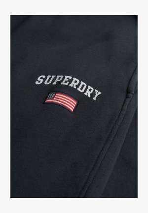 Dunkelblaues Sweatshirt mit weißem, gesticktem "SUPERDRY". Enthält ein Patch der amerikanischen Flagge mit roten, weißen und blauen Streifen.