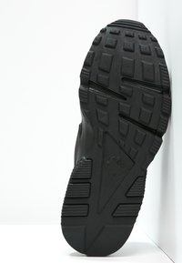 Svart sneakersula med texturerad gummi, med ett mönstrat mönster, framträdande knölar och en triangulär design i mitten.