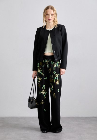 Sort cropped jakke med knapper, grøn ribbet crop top, sorte blomstrede vide bukser og en lille sort håndtaske. Glatte teksturer overalt.