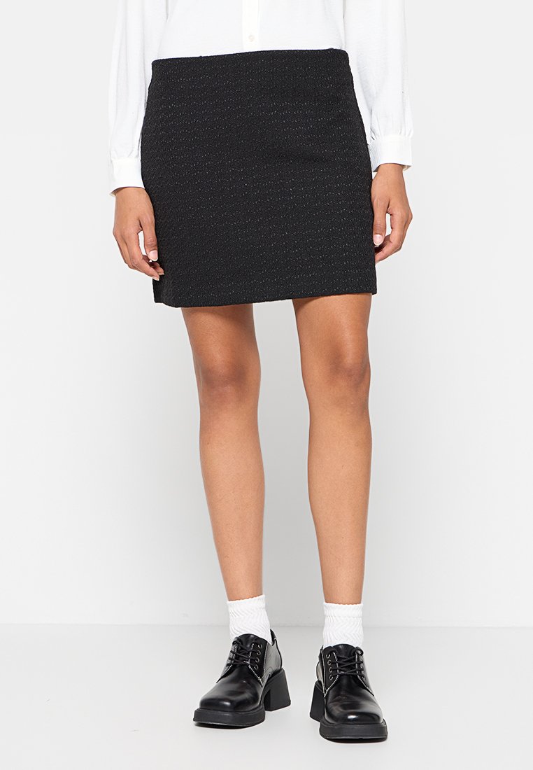 Zwarte, textuur geverfde mini-rok met een rechte silhouet, gecombineerd met zwarte schoenen en witte sokken. Gladde stof en subtiele patroonDetails.