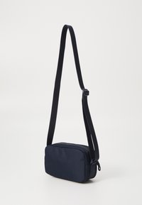 Mørkeblå rektangulær crossbody-veske laget av nylon, med justerbar stropp og glidelås. Glatt tekstur med minimal detaljering.