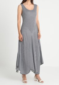 Długa sukienka bez rękawów w czarno-białe paski, z zaokrąglonym brzegiem, geometrycznym wzorem i lekkim materiałem. Do kompletu białe buty na słupku.