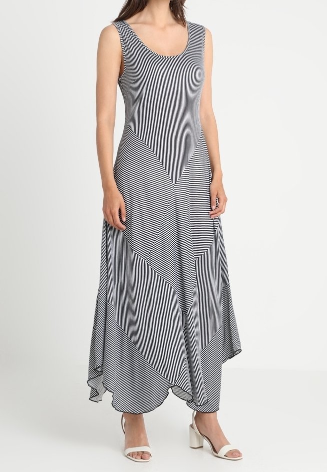 Długa sukienka bez rękawów w czarno-białe paski, z zaokrąglonym brzegiem, geometrycznym wzorem i lekkim materiałem. Do kompletu białe buty na słupku.