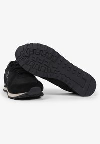 Zwarte sportieve schoenen met een bovenwerk van suede en textiel, met een getextureerde rubberen zool en een contrasterende off-white tussenzool.