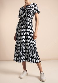 Svart- och vitmönstrad midiklänning med knytmidja, korta ärmar och sidospalter. Bärs med vita sneakers. Slät tygtextur.