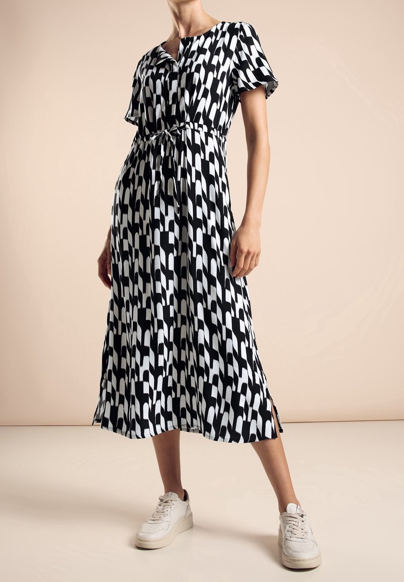Svart- och vitmönstrad midiklänning med knytmidja, korta ärmar och sidospalter. Bärs med vita sneakers. Slät tygtextur.
