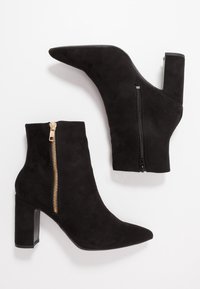 Botines de ante sintético negros con punta afilada, tacón alto en bloque y cremallera lateral con tirador de metal dorado.
