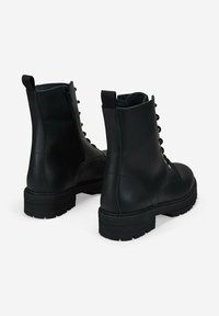 Un par de botas de combate de cuero negro con cordones, cremalleras laterales y suelas de goma gruesas sobre un fondo blanco.