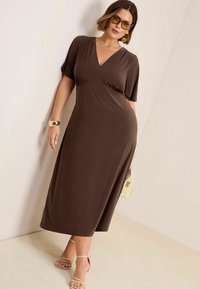 Braunes Midikleid mit V-Ausschnitt und kurzen, flatternden Ärmeln. Glatte Textur mit Raffung an der Taille. Abgerundet mit Riemchensandalen.