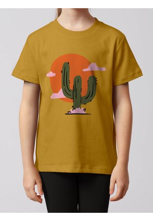 Enfant portant un t-shirt jaune moutarde arborant un cactus vert avec des épines noires sur un grand cercle orange et un arrière-plan de nuages roses.