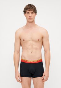 Boxeri negri, ajustați, cu un talie elastică lată în roșu și auriu, având logo-ul Nike. Țesătură netedă și elastică.