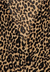 Gros plan sur un tissu plié avec un motif léopard marron et noir, montrant le tissage texturé et les coutures.