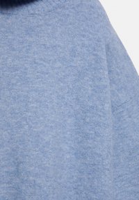 Puha, világoskék pulóver, texturált kötött anyagból, ribbelt nyakkivágással és laza sziluettel. Nincs látható fémrész vagy minta.