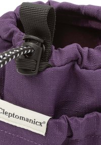 Purple fabric drawstring bag with a textured surface and a black adjustable strap. Features a visible brand tag for Cleptomanicx.