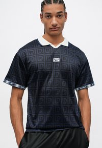 Cămașă polo Reebok în navy cu un model „R” pe tot materialul, guler alb și accente branduite pe mâneci, realizată dintr-un material ușor.
