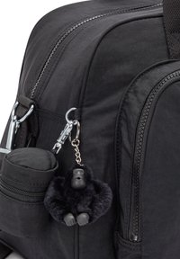 Black fabric backpack with dual zippers, a small round pocket, and a keychain featuring a black gorilla figure made of fuzzy material.