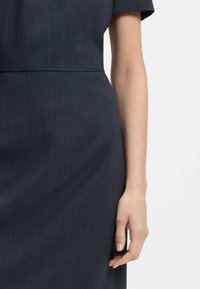 Navy blue dress featuring a textured fabric, short sleeves, and a fitted waist, with the hand resting on the fabric near the hem.