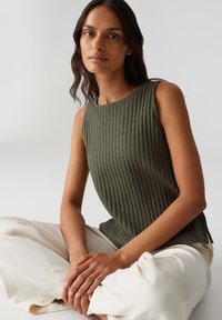 Top a manica corta color verde oliva a coste con scollo rotondo, design senza maniche e spacchi laterali, abbinato a pantaloni larghi di colore chiaro.