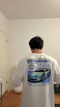 Hvit langermet t-skjorte med et blått grafisk trykk av en bil på baksiden, sammen med tekst og sirkulære logodesign.