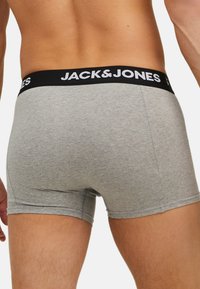 Boxer shorts en coton gris avec une taille noire arborant le nom de la marque "JACK&JONES" en blanc. Texture douce, design ajusté.